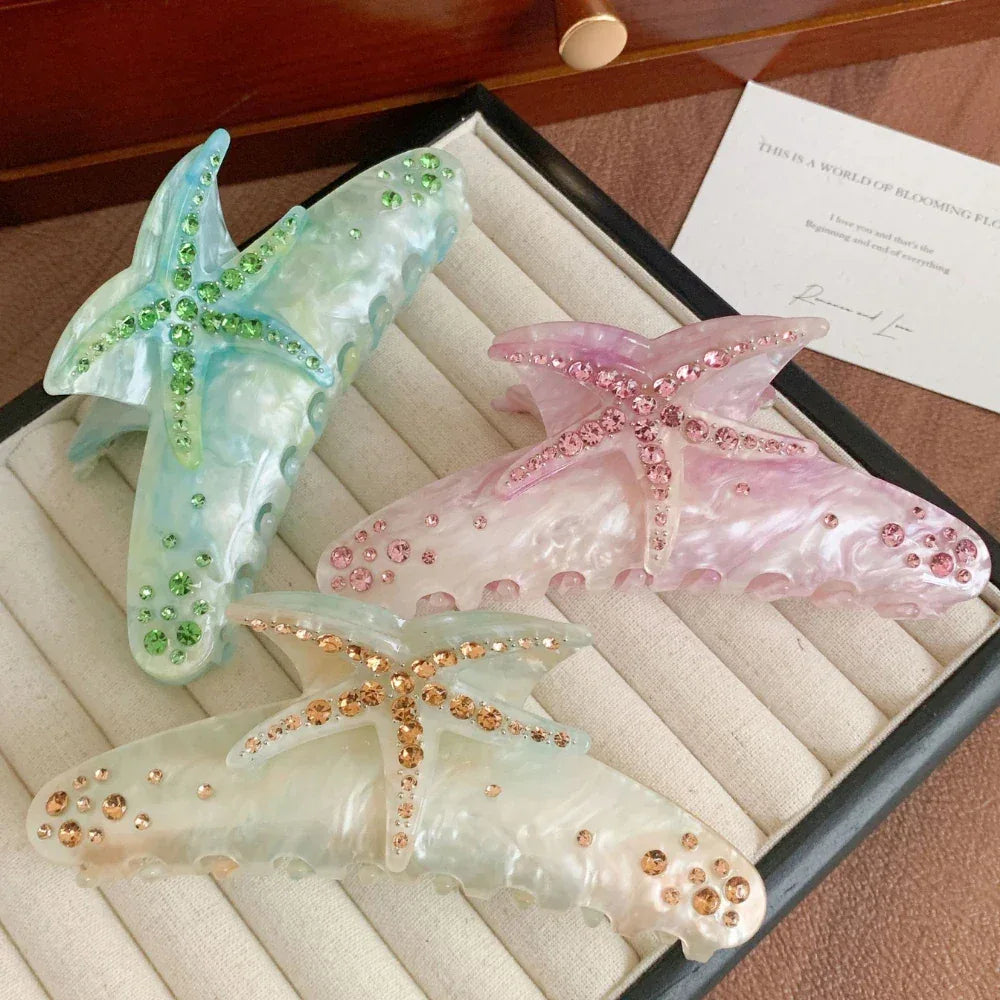 A collection of three colorful starfish-shaped hair claw clips, each embellished with sparkling rhinestones, displayed within a velvet-lined box.
