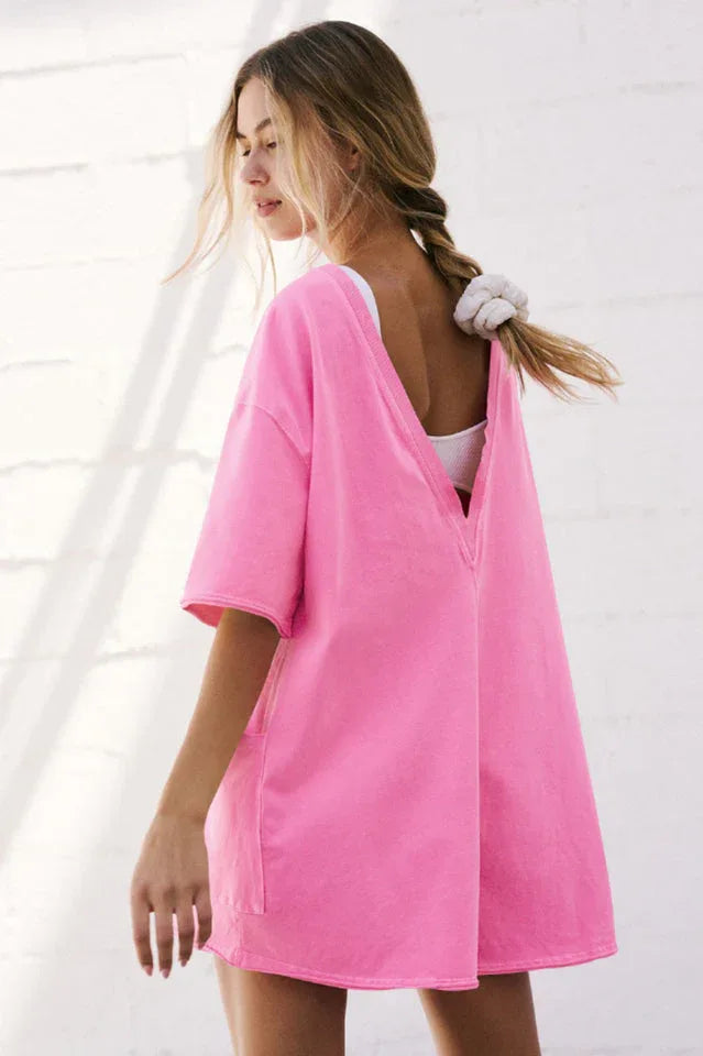 Back view of a woman wearing a bright pink oversized tunic, showing a deep V-neckline.