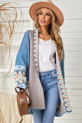 Woman wearing a long blue open-front cardigan with geometric print details, a white tank top, blue jeans, and a tan hat.
