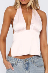 Woman wearing a light pink satin halter top with a deep V-neck and blue jeans.