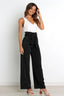 Woman wearing high-waisted wide-leg black pants with a white tank top and heels.