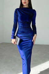 Woman wearing a royal blue long-sleeved velvet bodycon midi dress with ruching detail, holding a silver clutch and wearing silver heels.