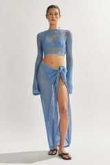 Model wearing a blue sheer knit cropped long-sleeve top, bikini, and a matching blue sheer knit maxi skirt with a high slit.