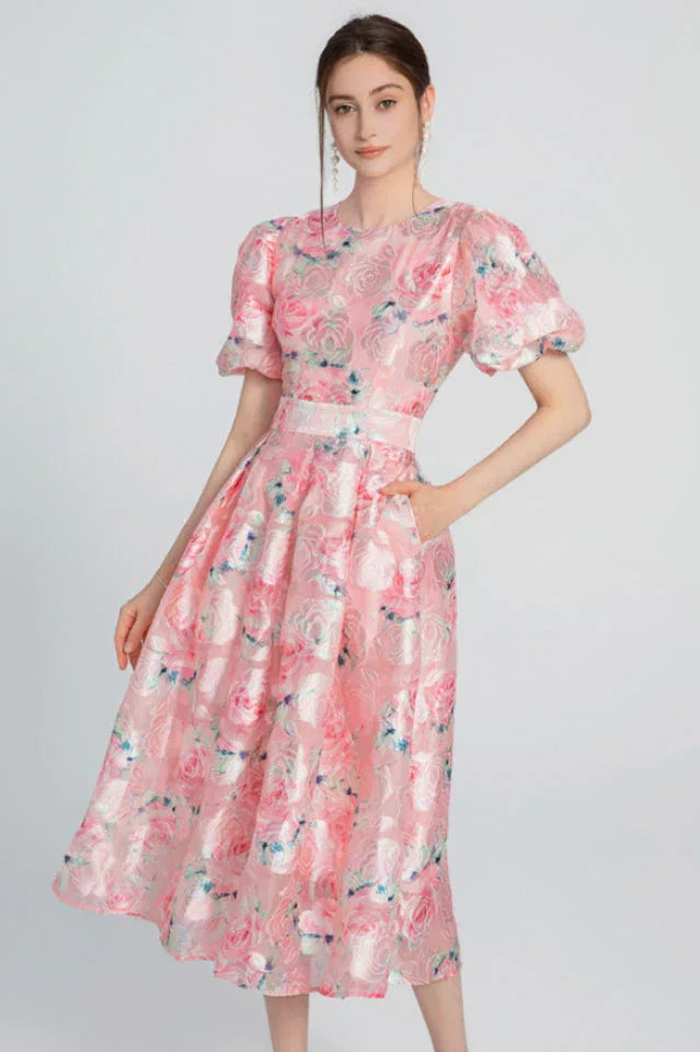Woman wearing a pink floral jacquard midi dress with puff sleeves and a belted waist.
