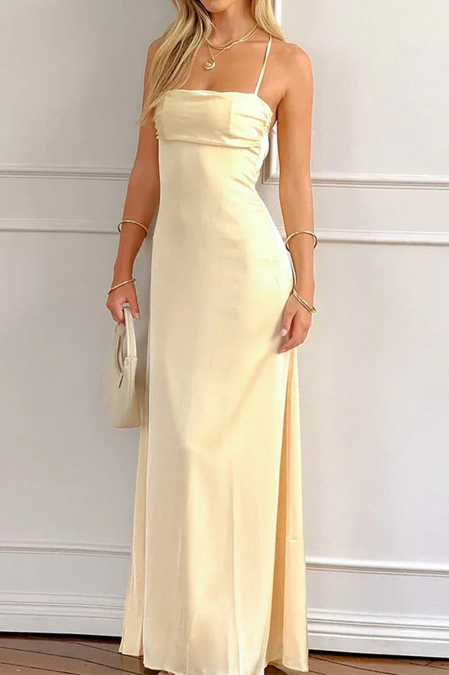 woman wearing a pale yellow satin maxi dress with spaghetti straps, holding a small white handbag