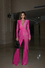 Woman in a bright pink jumpsuit with sequin accents, holding a black handbag.