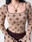 Close-up of a fitted, long-sleeved square neck top with an allover brown floral print on a beige textured knit fabric. The neckline and sleeve cuffs have dark scalloped trim. A butterfly pendant necklace is worn.
