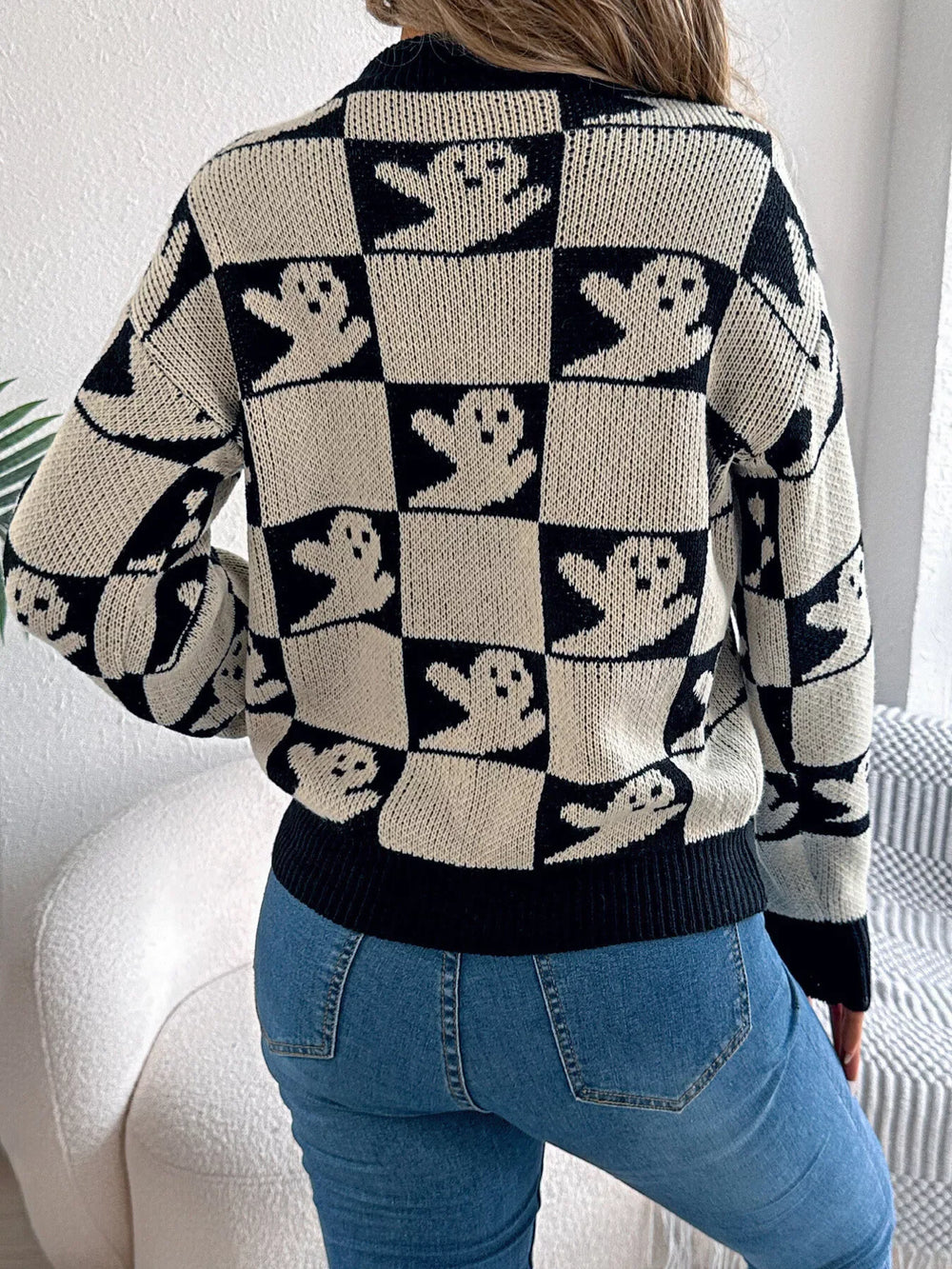 Back view of a woman wearing a black and white ghost print checkerboard knit sweater with blue jeans.