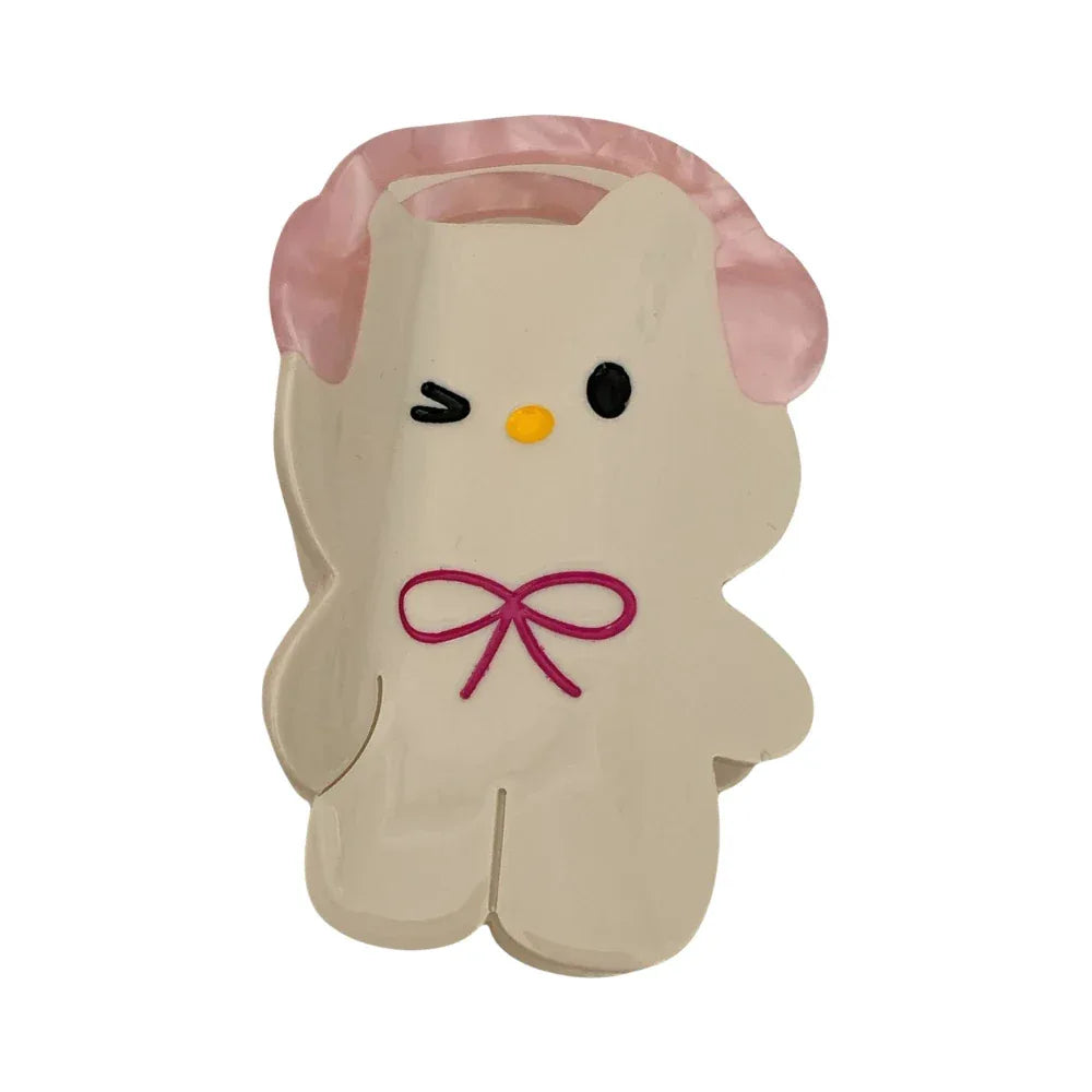 Close-up of a white cartoon character hair clip with pink headphones and a pink bow.