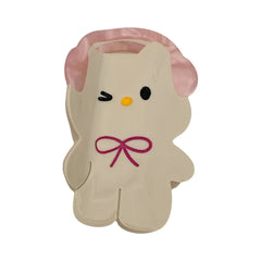 Close-up of a white cartoon character hair clip with pink headphones and a pink bow.