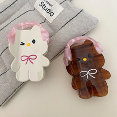 Two cartoon character hair clips, one white and one brown, on a grey textured surface with a studio tag.