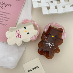 Two cartoon character hair clips, one white and one brown, lying on a white surface next to a pink card.