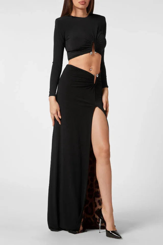 Full body shot of a woman wearing a black long-sleeve crop top and a black maxi skirt with a high slit and leopard print lining, against a white background.