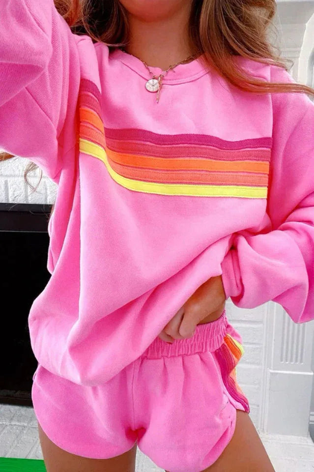 Front view of a woman wearing a pink sweatshirt with rainbow stripes and matching shorts.
