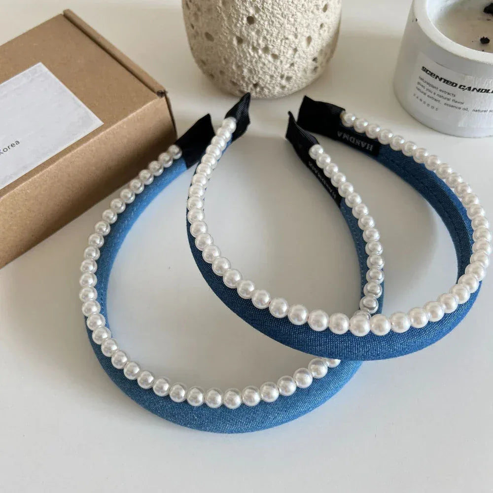 Pair of blue denim headbands with pearl trim on a white surface