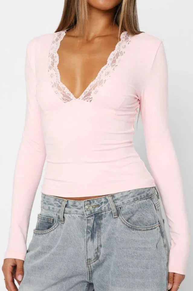 Close-up of a woman wearing a pink long-sleeved top with lace trim and blue jeans, front view