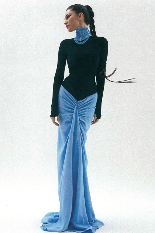 Woman wearing a black long-sleeved top and a light blue draped skirt with a high neckline and braided hair