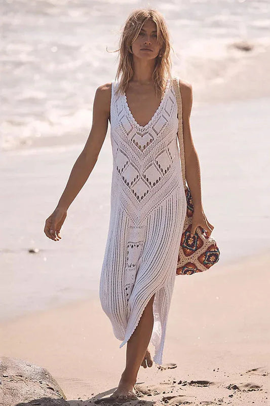 woman wearing a white crochet knit midi dress with side slits and a straw bag on the beach