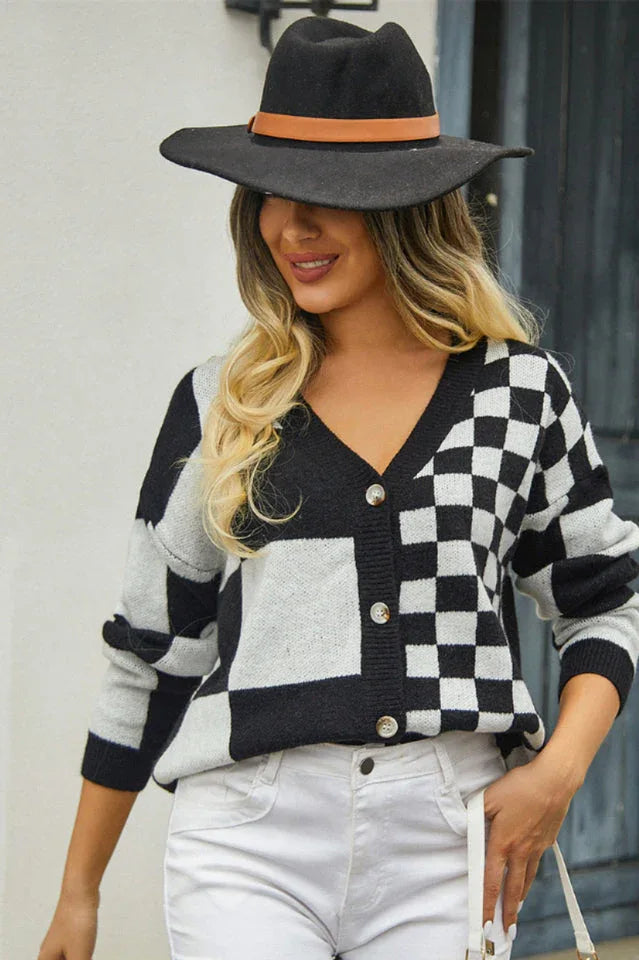 Woman wearing a black and white checkerboard print cropped cardigan, white jeans, and a black hat, holding a coffee cup.