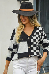 Woman wearing a black and white checkerboard print cropped cardigan, white jeans, and a black hat, holding a coffee cup.