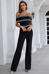 Full body shot of a woman in a black off-the-shoulder jumpsuit with geometric trim.