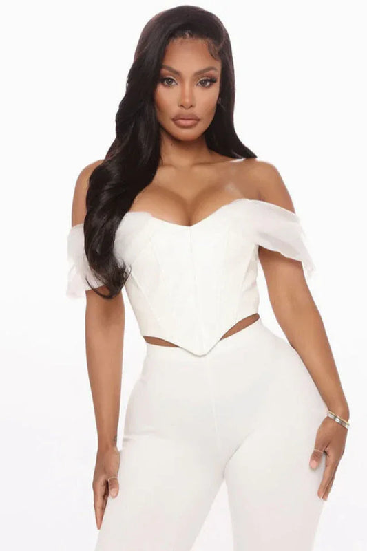 Woman wearing a white off-the-shoulder corset top with sheer sleeves and white pants