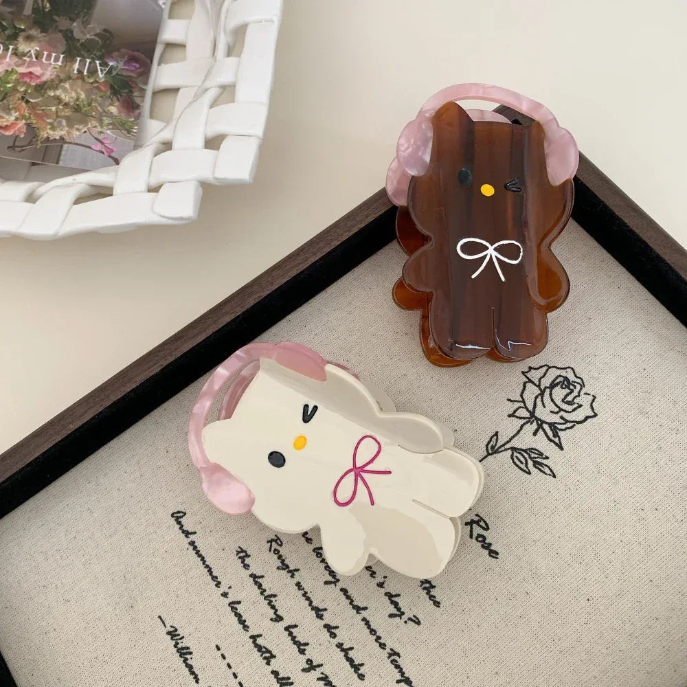 Two cartoon character hair clips, one white and one brown, arranged on a framed canvas with a floral sketch.