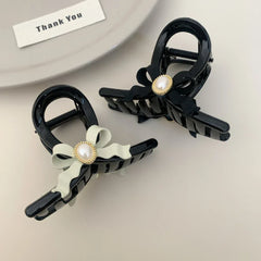 Two black hair claw clips with pearl accents, one with a black bow and one with a light green bow, on a plate