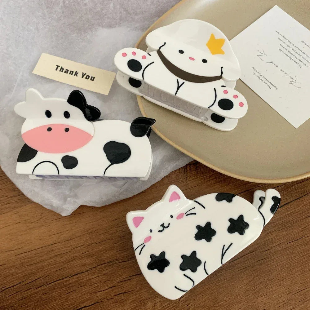 A close-up view of three animal-shaped hair clips: a cow, a dog, and a cat, displayed on a tray with decorative elements.