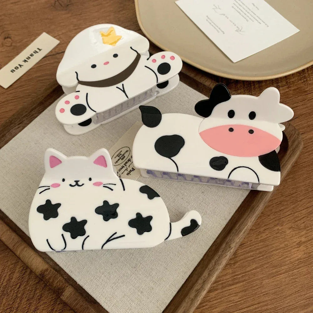 Three adorable animal-themed hair clips - a cow, a dog, and a cat - are showcased on a wooden surface.