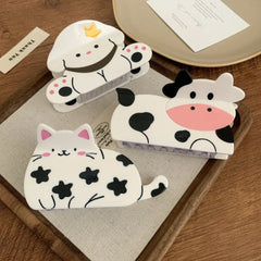 Three adorable animal-themed hair clips - a cow, a dog, and a cat - are showcased on a wooden surface.