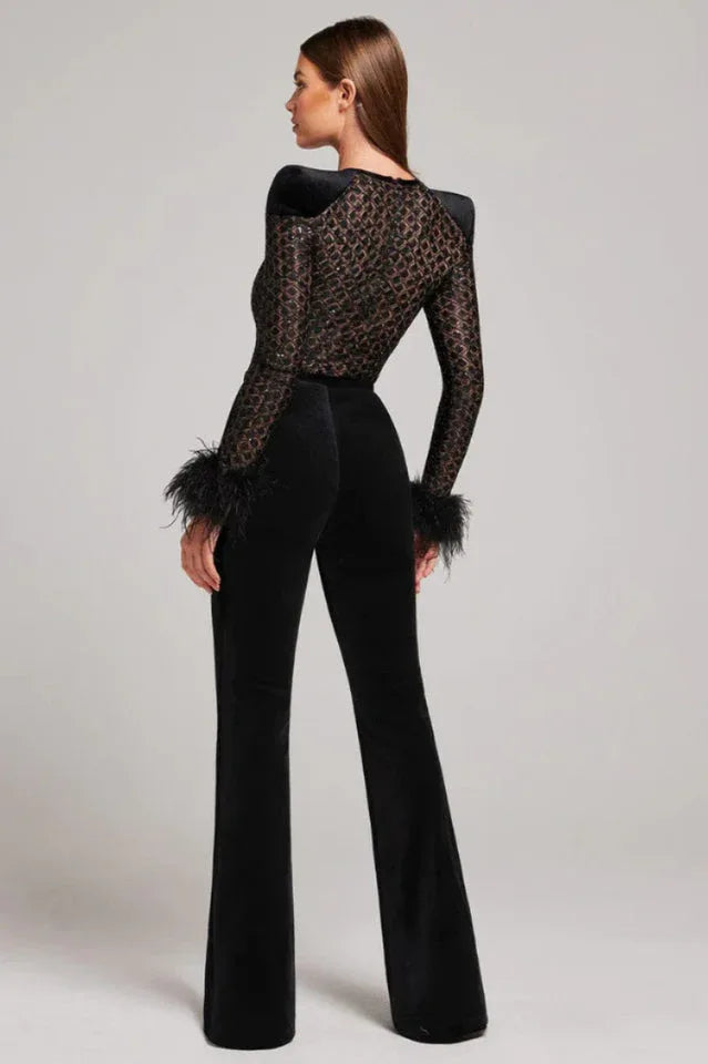 Woman modeling a black sequined mesh top with feathered cuffs and black velvet flared pants from the back.