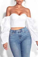 Woman wearing a white off-the-shoulder crop top with puff sleeves and blue jeans, front view
