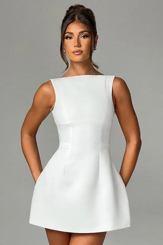 Woman wearing a white sleeveless boat neck mini dress with her hands in her pockets.