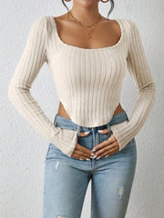 Woman wearing a cream-colored ribbed long-sleeve crop top and light-wash denim jeans, with her hands clasped in front of her.