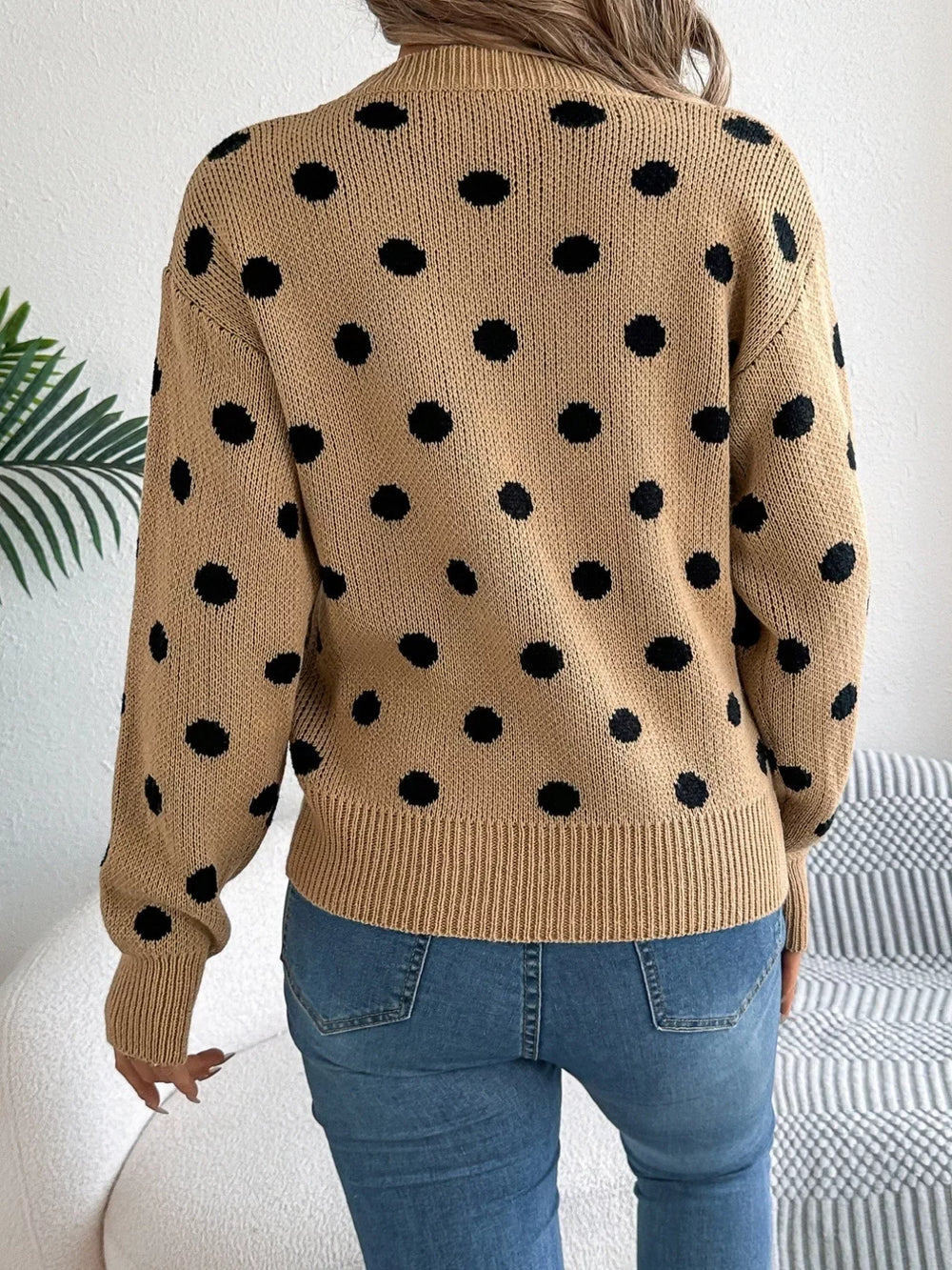 Woman wearing a brown polka dot sweater with blue jeans, back view.