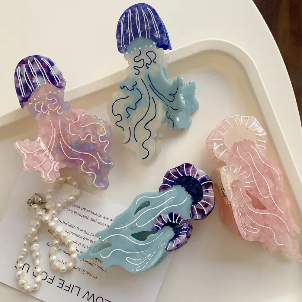 Four acrylic jellyfish hair clips, including pink, purple, blue, and light pink, arranged on a white tray with a pearl necklace.