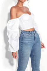 Woman wearing a white off-the-shoulder crop top with puff sleeves and blue jeans, side view