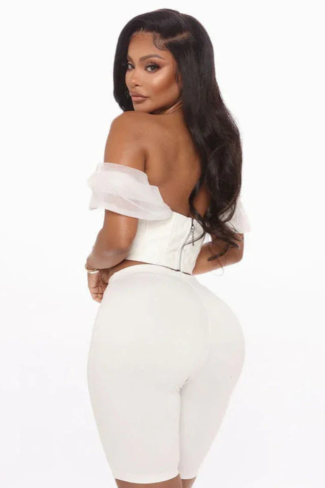 Back view of a woman in a white off-the-shoulder corset top and white pants