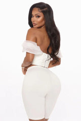 Back view of a woman in a white off-the-shoulder corset top and white pants