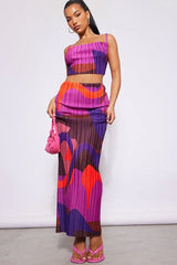 Woman wearing a vibrant abstract print pleated crop top and maxi skirt set with pink accessories.