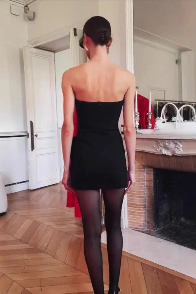 Back view of a model wearing a black strapless mini dress with black sheer tights.