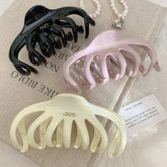 three octopus claw hair clips in black, pink, and cream arranged on a textured surface