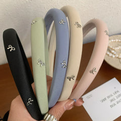 Collection of padded headbands in black, sage green, sky blue, beige, and blush pink, each adorned with small silver bow charms