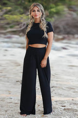 Woman wearing a black crop top and wide leg pants on a beach