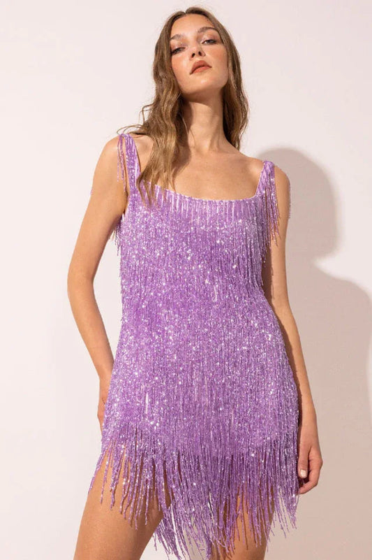 Model wearing a sparkly purple mini dress with fringe detailing, front view