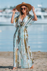 Full-length shot of a woman on a beach wearing a light, airy maxi dress with a watercolor print, a deep V-neck, and a straw hat.