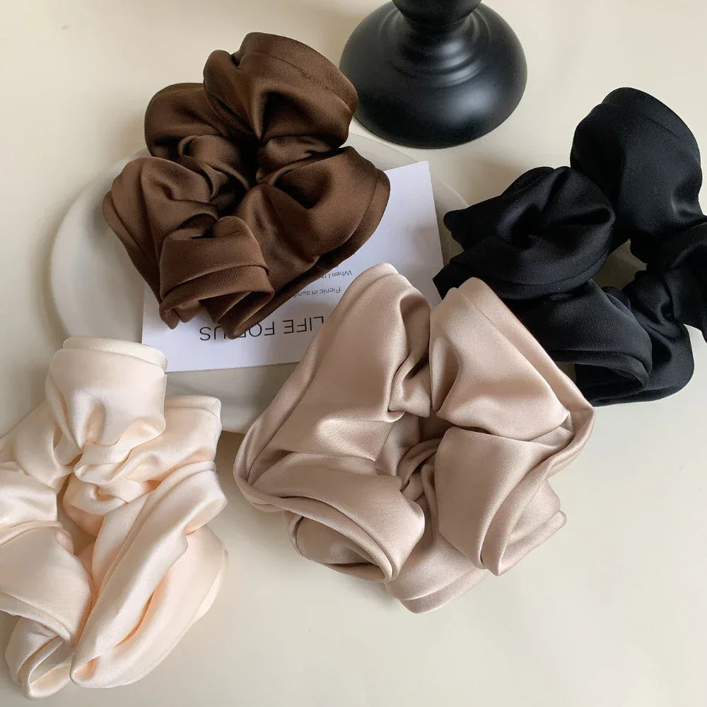 four scrunchies in brown, black, beige, and cream arranged on a surface