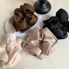 four scrunchies in brown, black, beige, and cream arranged on a surface