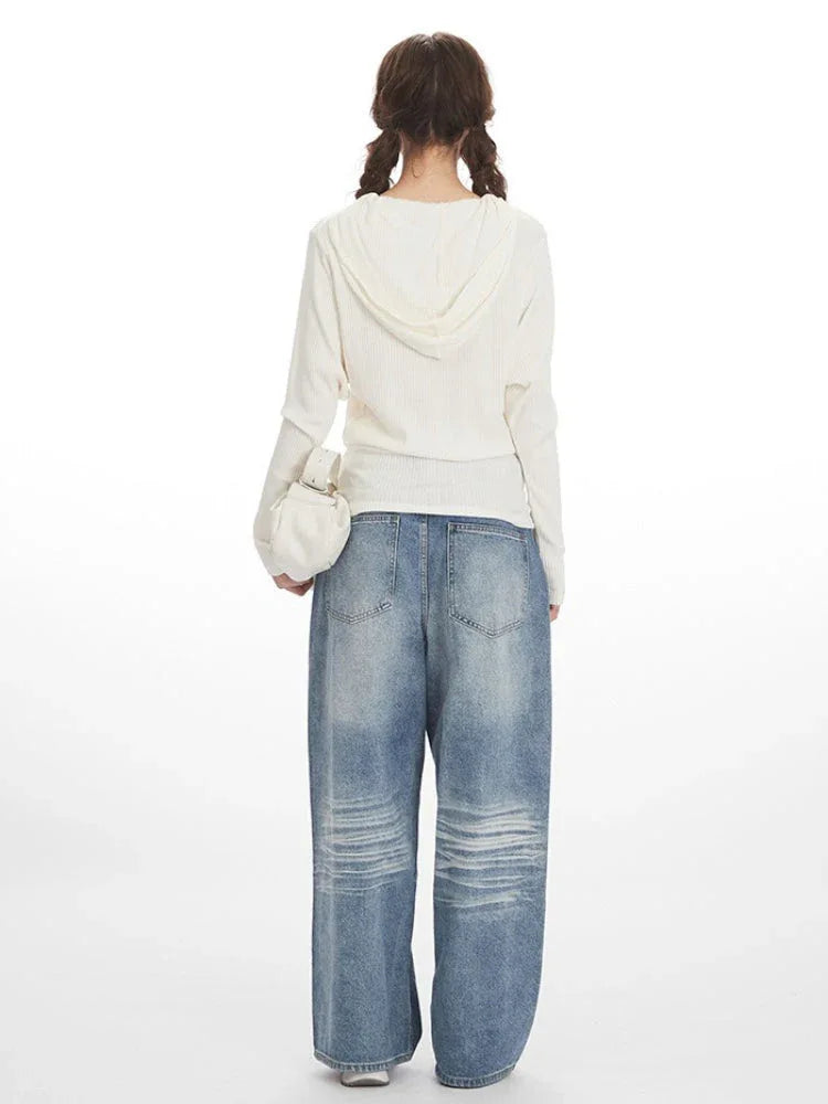 Back view of a woman wearing a white ribbed knit long-sleeve shirt and distressed wide-leg blue jeans.